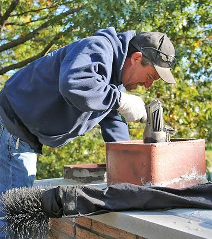 Technician examining a chimney cap and sweeping equipment on a roof